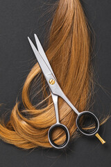 Top view of scissors and a cut off strand of children's blond hair on a dark paper background