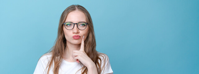 Worried stupid and insecure young woman with long hair nervous fingers in alarm and panic, frowning with a worried expression in a white t-shirt on a blue background in the studio - obrazy, fototapety, plakaty