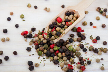 mixed whole peppercorns on a light wooden surface with a wooden scoop