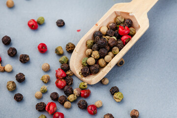 mixed whole peppercorns on a grey surface with wooden scoop