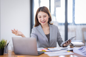 Business Asian woman using calculator and writing make note with calculate doing math finance on an office desk. Woman working at office with laptop and tax, accounting, documents on desk.