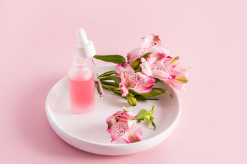 an open matte white bottle with a filled pipette of natural moisturizer facial skin care stands on a white ceramic plate. pink background.