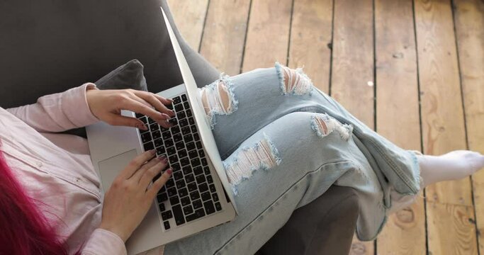 Close-up of a woman's legs working with her laptop while sitting on a chair on a veranda with a wooden floor. Top view. Home office concept.