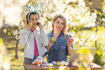 mother and daughter paint easter eggs with laptop, record lessons on a webcam with a laptop. mother and daughter are preparing for the holiday together.