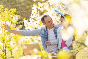 father and daughter coloring easter eggs with laptop in the garden