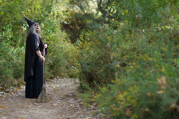 white-haired witch with her broom on a forest trail