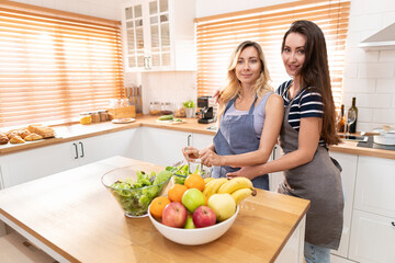 Happy same sex couple feed each other at kitchen. Cheerful LGBTQ lesbian woman feeding salad each other. A beautiful couple of lesbian ladies having a romantic moment in the kitchen.