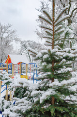 spruce covered with snow against the background of a children's cloak in the park and the winter sky