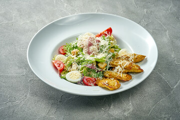Classic caesar salad with sauce, grilled chicken and vegetables in a white plate. Concrete background