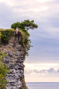 Adult woman sitting alone on edge of coastal cliff, Bali, Indonesia