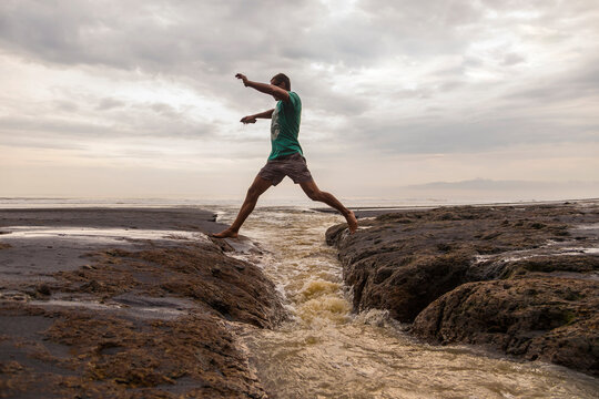 Man jumping over coastal water at beach, Bali, Indonesia