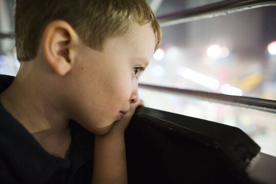 Young boy rests his head on ride at fairground while quietly looking