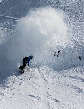 Professional Snowboarder Chris Coulter Does A Powder Slash And Rides Through The Cloud On A Sunny Day