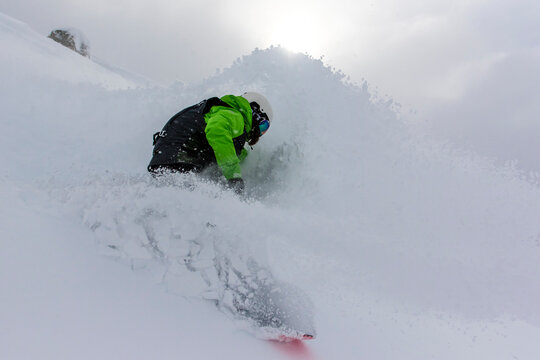 A Female Snowboarder Makes A Turn In Deep Powder Snow And Nearly Covers Herself With Blowing Snow On A Stormy Day In Bounds At Cerro Catedral In Argentina.