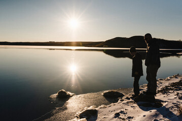 Father and son stand on the edge of freezing lake during winter