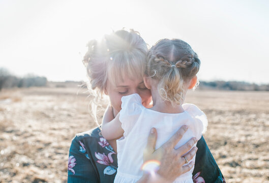 mother holding her daughter whilst standing in a field at sunset