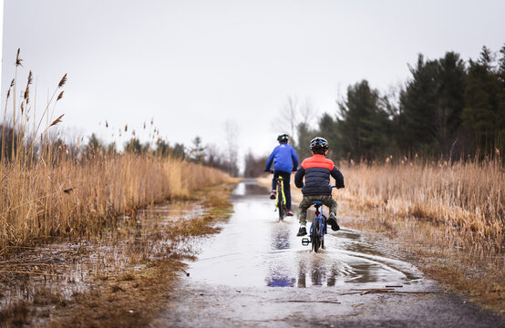 Two boys riding their bikes through a large puddle on a flooded trail.