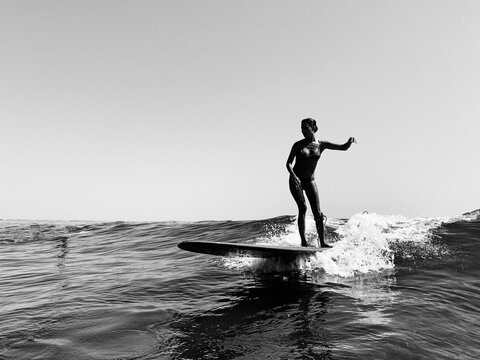 Fototapeta A female surfer in a bikini rides a small wave, black and white