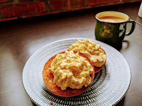 egg salad begal and a cup of coffee on a wooden table