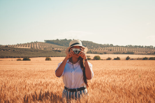 Young woman taking photos with a vintage photo camera in a wheat field