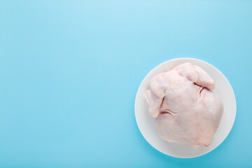 White plate with fresh raw hen meat on light blue table background. Pastel color. Closeup. Empty place for text. Top down view.