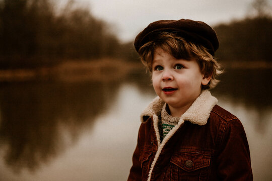 young boy in newsboy cap in front of pond