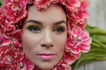 The face of beautiful woman with colorful make-up and flowers . The attractive woman lies in tulips.