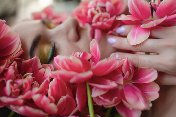 Portrait of a girl with good skin,perfume and cosmetics conceptThe face of beautiful woman with colorful make-up and flowers . The attractive woman lies in tulips.