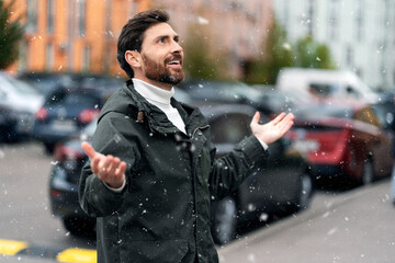 Side view of happy man holding hands open, watching snow fall. Smiling man looking up outdoors.