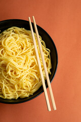 egg noodle on a black bowl. wooden chopstick. brown background