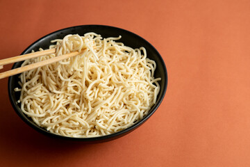 egg noodle on a black bowl. hold with wooden chopstick. brown background