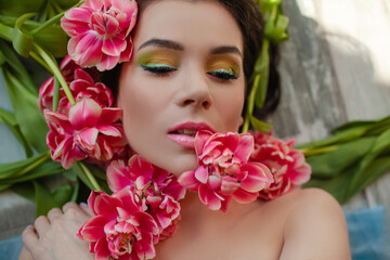Portrait of a girl with good skin,perfume and cosmetics conceptThe face of beautiful woman with colorful make-up and flowers . The attractive woman lies in tulips.