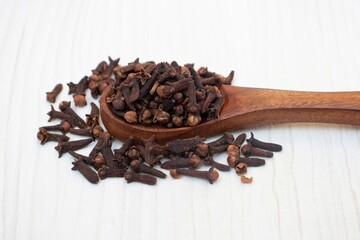 Dry Cloves in a Wooden Spoon Isolated on White Wooden Background