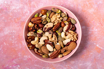 Viewed from above, against a textured background, an isolated bowl holds a large variety of shelled nuts.