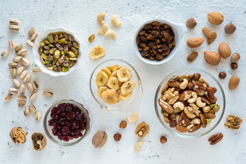 Top view, close-up, on a textured white concrete background, some bowls with mixed dried and dehydrated fruits