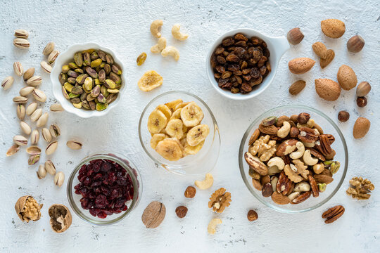 Top view, close-up, on a textured white concrete background, some bowls with mixed dried and dehydrated fruits