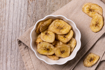 Top view, extreme close-up, on a textured wooden background, a bowl with dehydrated banana chips