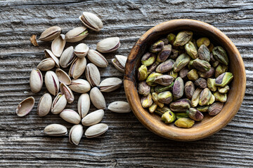 Top view, on an old wooden background, extreme closeup, a pile of pistachios and a bowl with...