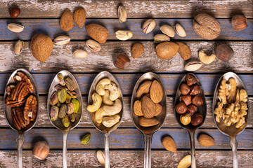 top view, on a wooden background, a composition of mixed and shelled dried fruits is arranged in six vintage spoons,