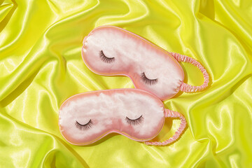 Creative layout with two pastel pink sleep masks with false eyelashes on neon yellow satin background. 80s or 90s retro fashion aesthetic concept. Minimal romantic cosmetic beauty Valentines day idea.