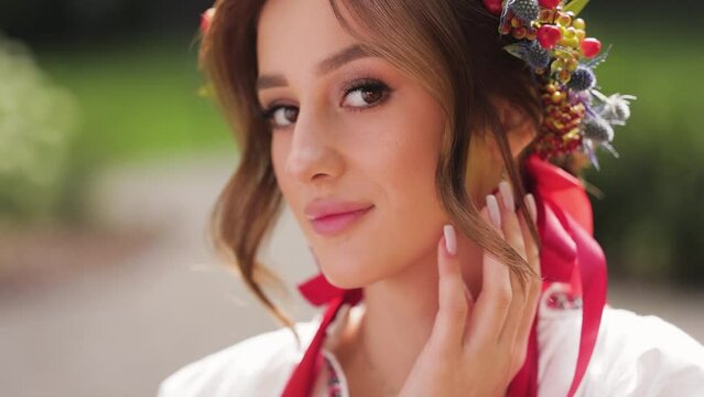 Close up Portrait of Beautiful bride dressed in ukrainian ethno clothes. Woman in a wreath of flowers standing in the park. Morning of the bride concept. Medium shot
