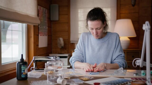 young woman makes handmade earrings of polymer clay sitting at table at home. self taught artist creates craft jewellery