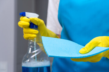 Close-up of a woman in uniform and yellow rubber gloves holding detergent and a microfiber cloth. Cleaning the apartment and demonstration of spray and cleaning products. Cleaning company