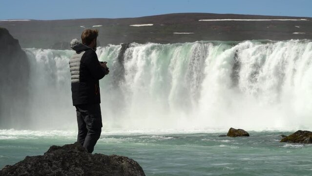 Male photographer approaches glacial Iceland Godafoss waterfall to take closeup
