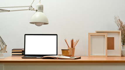 Comfortable home office interior with laptop computer, lamp, photo frame and stationery on wooden desk