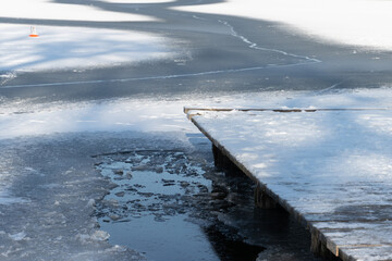 Broken thin ice on a lake beside a pier covered with snow