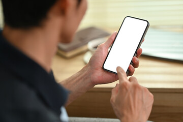 Young man hand checking social media on mobile phone. Over shoulder closeup view, blank screen for graphic display montage