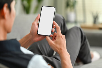 Over shoulder view of relaxed man sitting on couch and using smart phone. People, technology and lifestyle concept