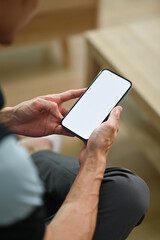 Relaxed man sitting on couch at home and checking social app on smart phone. Close up view