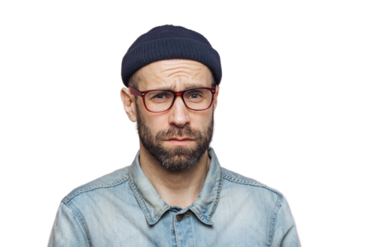 Grumpy bearded man with offended expression, being dissatisfied with something, frowns face, wears spectacles, hat and shirt, isolated over pink background. Displeasure and negativity concept
